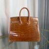 Miel Shiny Niloticus Crocodile Birkin 25 Retourne Gold Hardware Front view of a Birkin 25 bag in Miel shiny Niloticus crocodile leather with gold hardware.