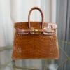 Miel Shiny Niloticus Crocodile Birkin 25 Retourne Gold Hardware Front view of a Birkin 25 bag in Miel shiny Niloticus crocodile leather with gold hardware.